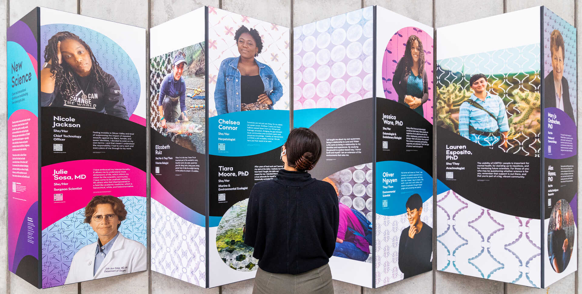 Guest looks at New Science exhibit panel featuring portraits of LGBTQ+ scientists