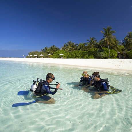 2 guests learn how to scuba dive with an instructor in the crystal clear waters of the Maldives
