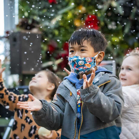 Masked and unmasked kids frolic under indoor snow flurries in the Academy Piazza