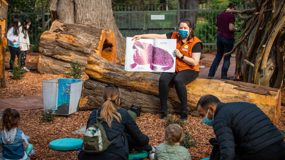 An Academy presenter reads a storybook to children outdoors in Wander Woods