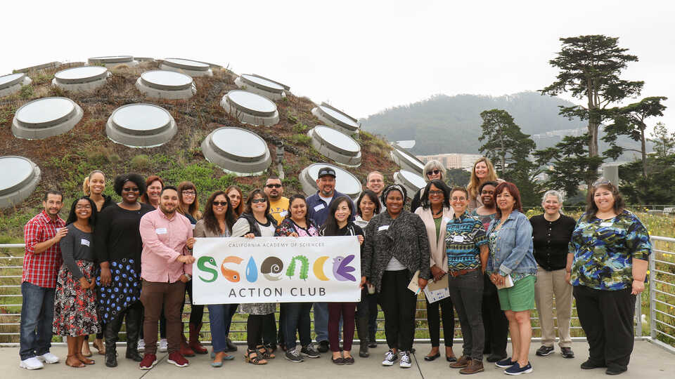 Group of Science Action Club educators holding SAC banner atop Academy Living Roof